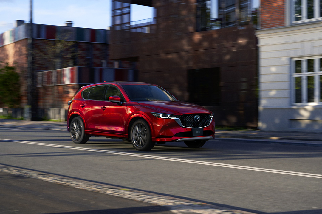 Red 2025 Mazda CX-5 SUV driving down a city street