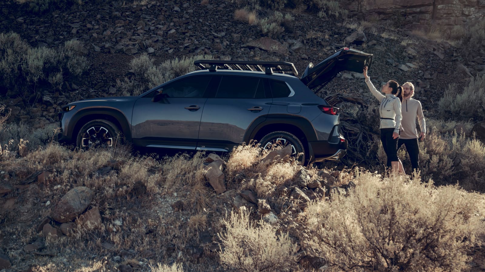 A smiling couple opening the rear liftgate of the 2025 Mazda CX-50 SUV
